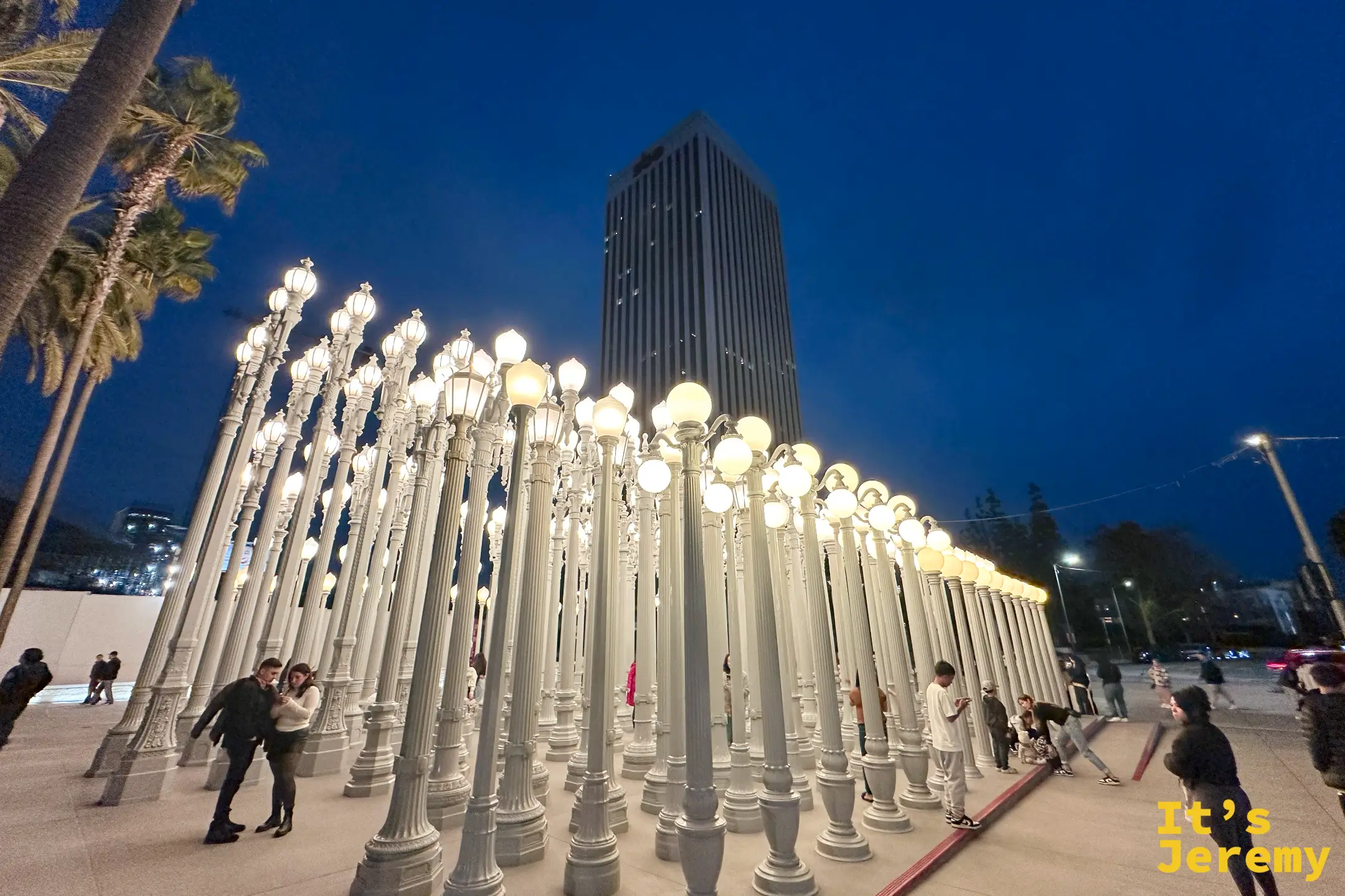 藍調時刻的 Urban Light，燈林後方是黑色的 LACMA 大樓與棕櫚樹
