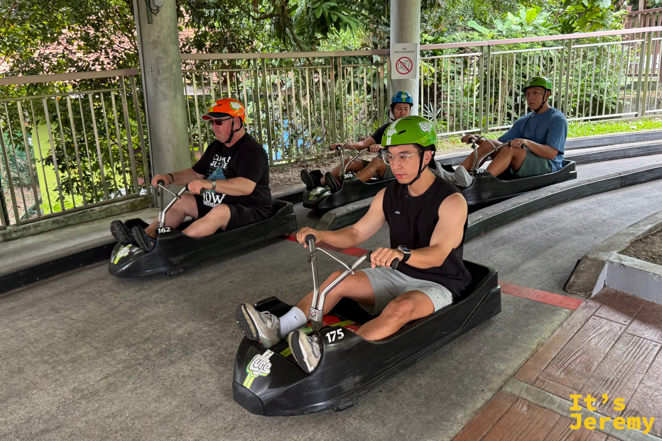 數名遊客駕駛無動力三輪滑車在聖淘沙的水泥下坡賽道上極速衝刺
