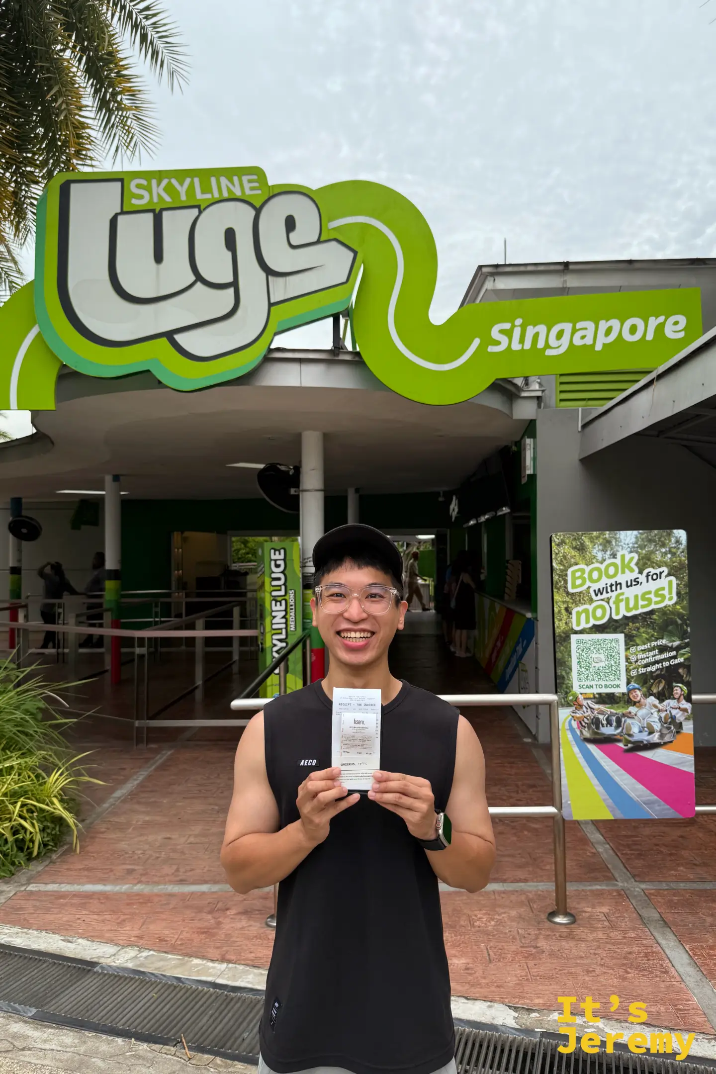 遊客站在亮綠色的 Skyline Luge Singapore 官方招牌與購票櫃檯前手拿票券留影