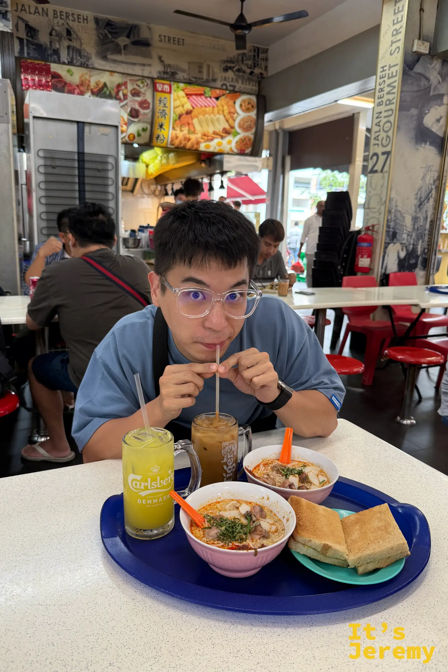 男遊客坐在咖啡店內，正準備品嚐剛端上桌的炭燒叻沙，桌上還有冰咖啡與果汁