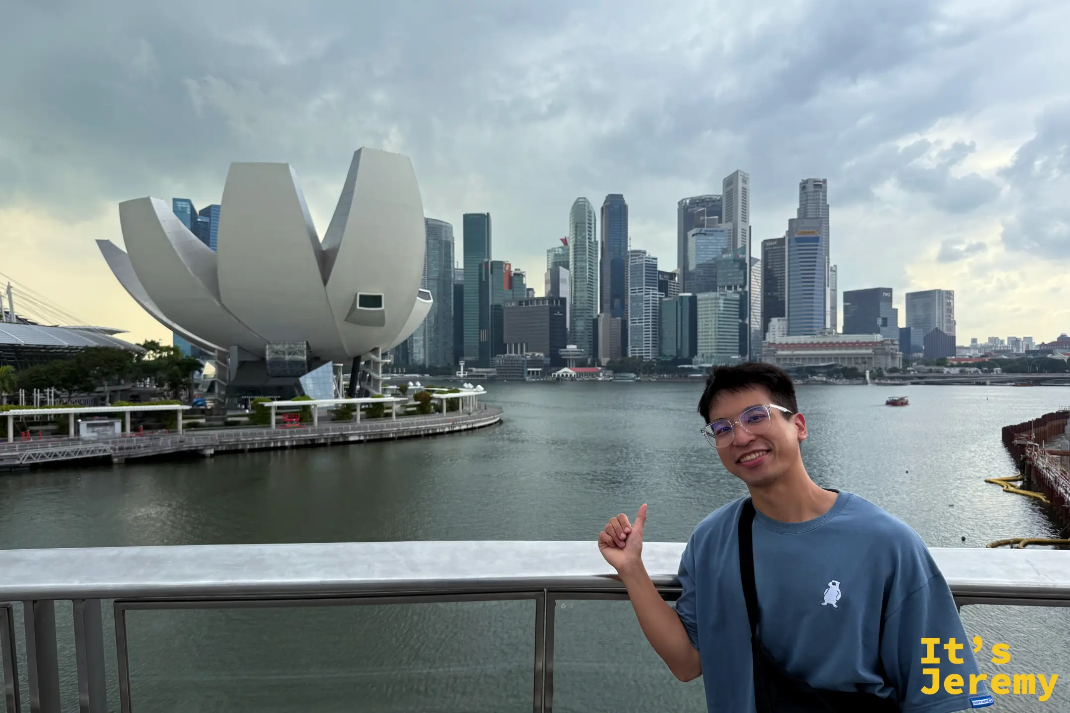 遊客站在摩天輪下方海濱步道合影,背景是濱海灣金沙、蓮花造型的藝術科學博物館與金融區高樓