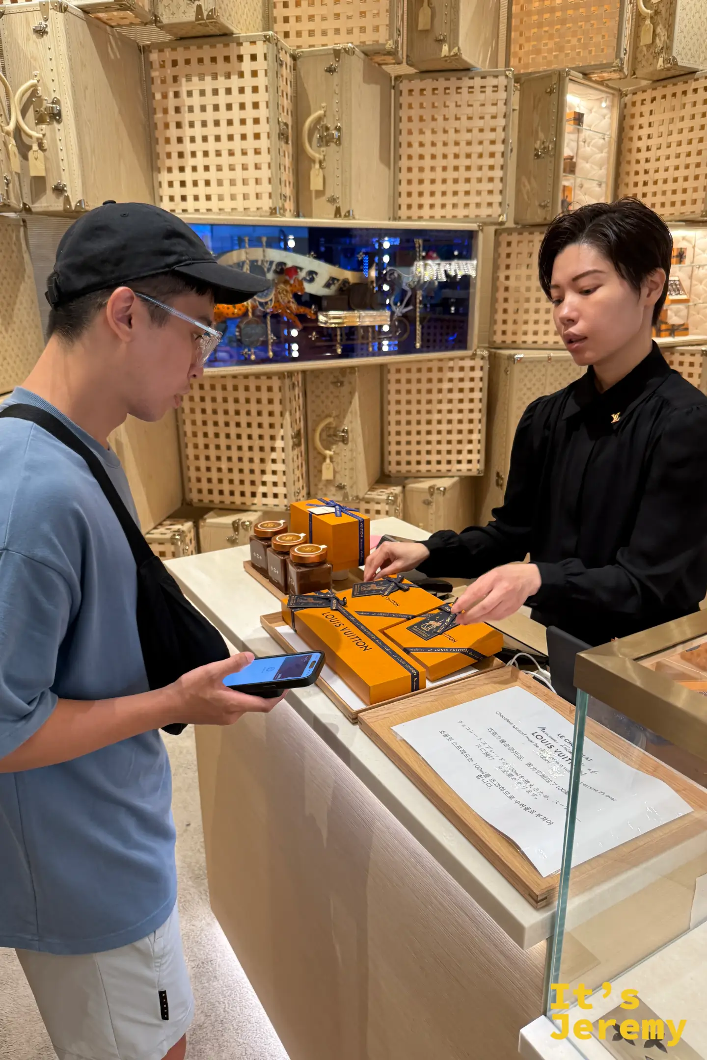 一名男遊客在金色工作檯前,一邊聽身穿黑襯衫的店員專業解說,一邊挑選印有 Monogram 標誌的手工巧克力系列