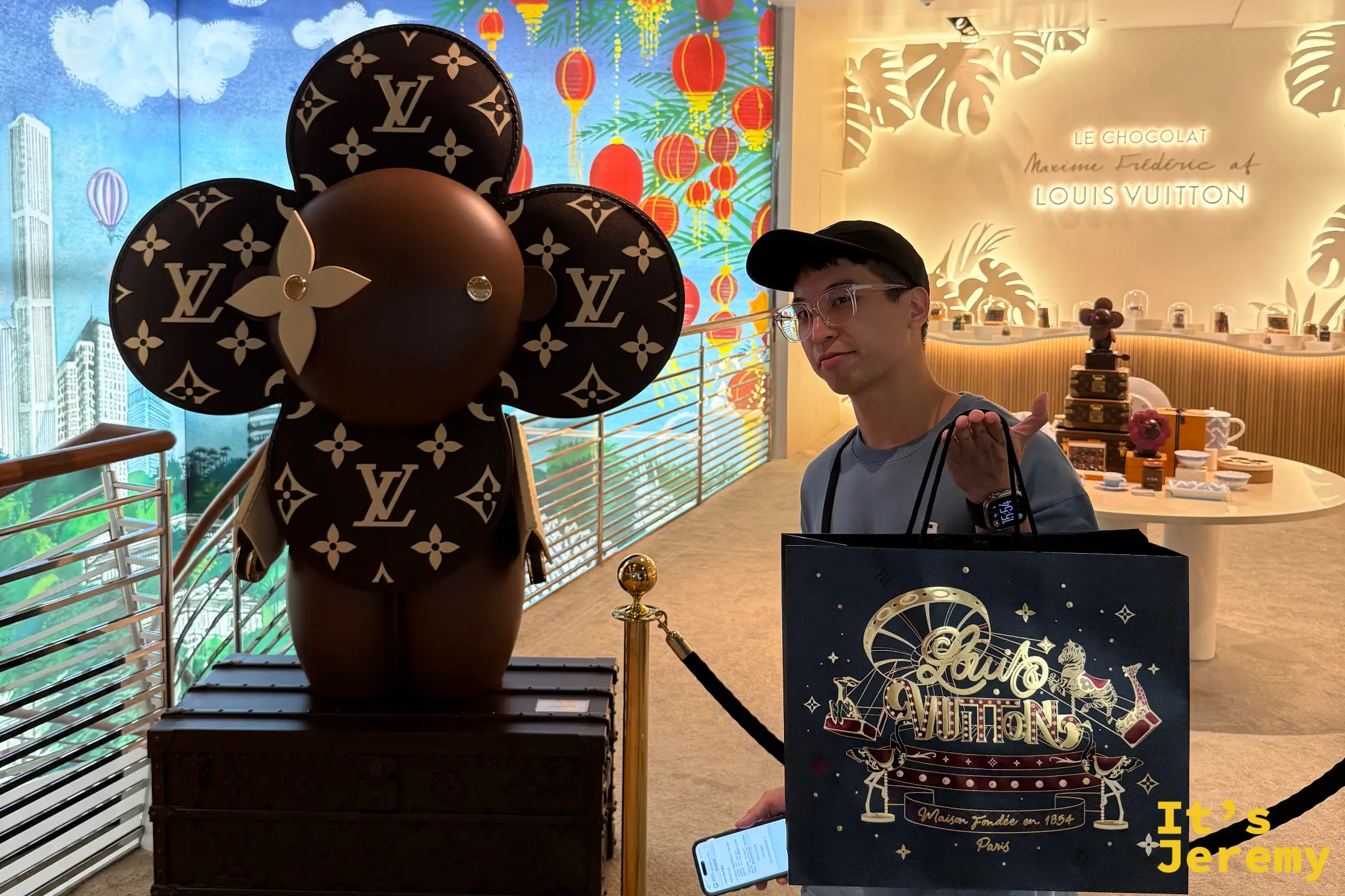 遊客手拿奢華的 LV 紙袋與黑金色新年限定包裝盒,在店門口巨大的 Monogram 老花 Vivienne/Petula 巧克力雕塑旁打卡,背景是絢麗的數位藝術光雕