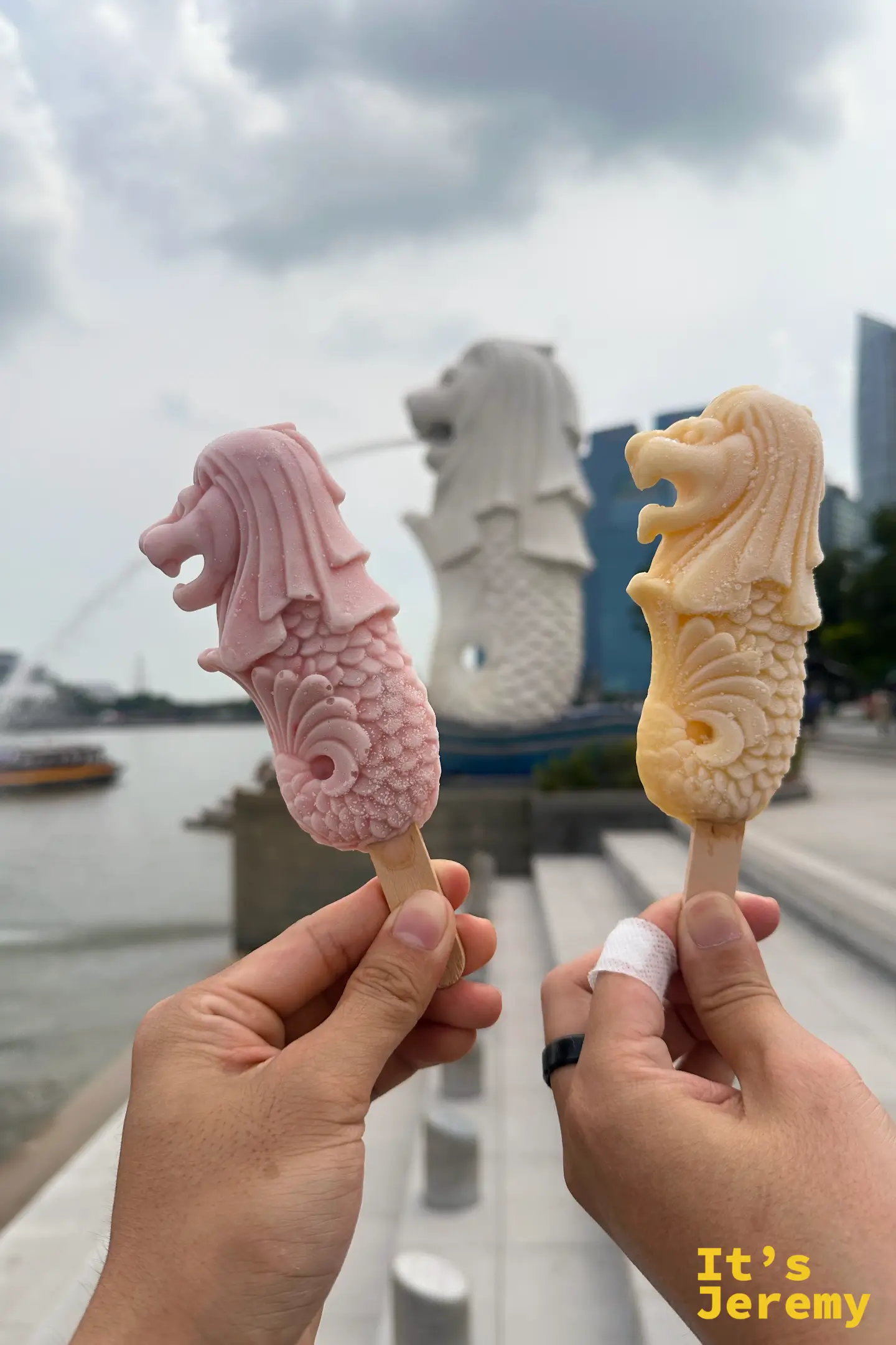 雙手同時拿著兩枝不同口味的魚尾獅造型冰棒——粉紅色與奶茶啡色,在台階前展示這款兼具視覺與美味的冰品
