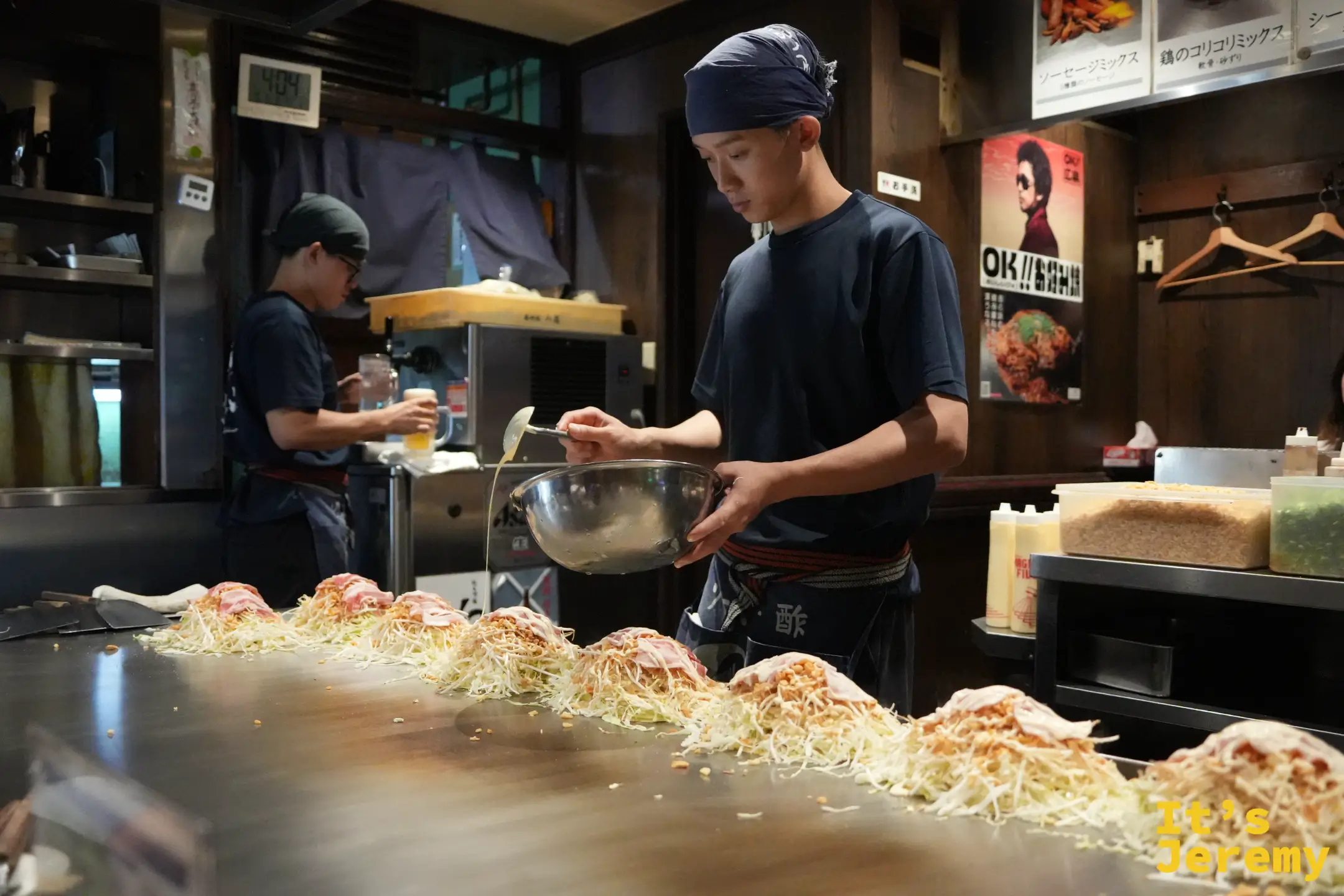 店員一手捧著麵糊盆、一手拿湯勺，在鐵板上攤開餅皮