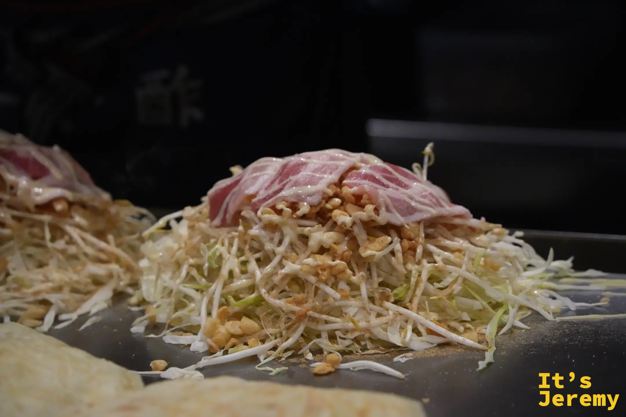 堆滿豆芽菜與高麗菜的廣島燒，上面鋪著豬肉片