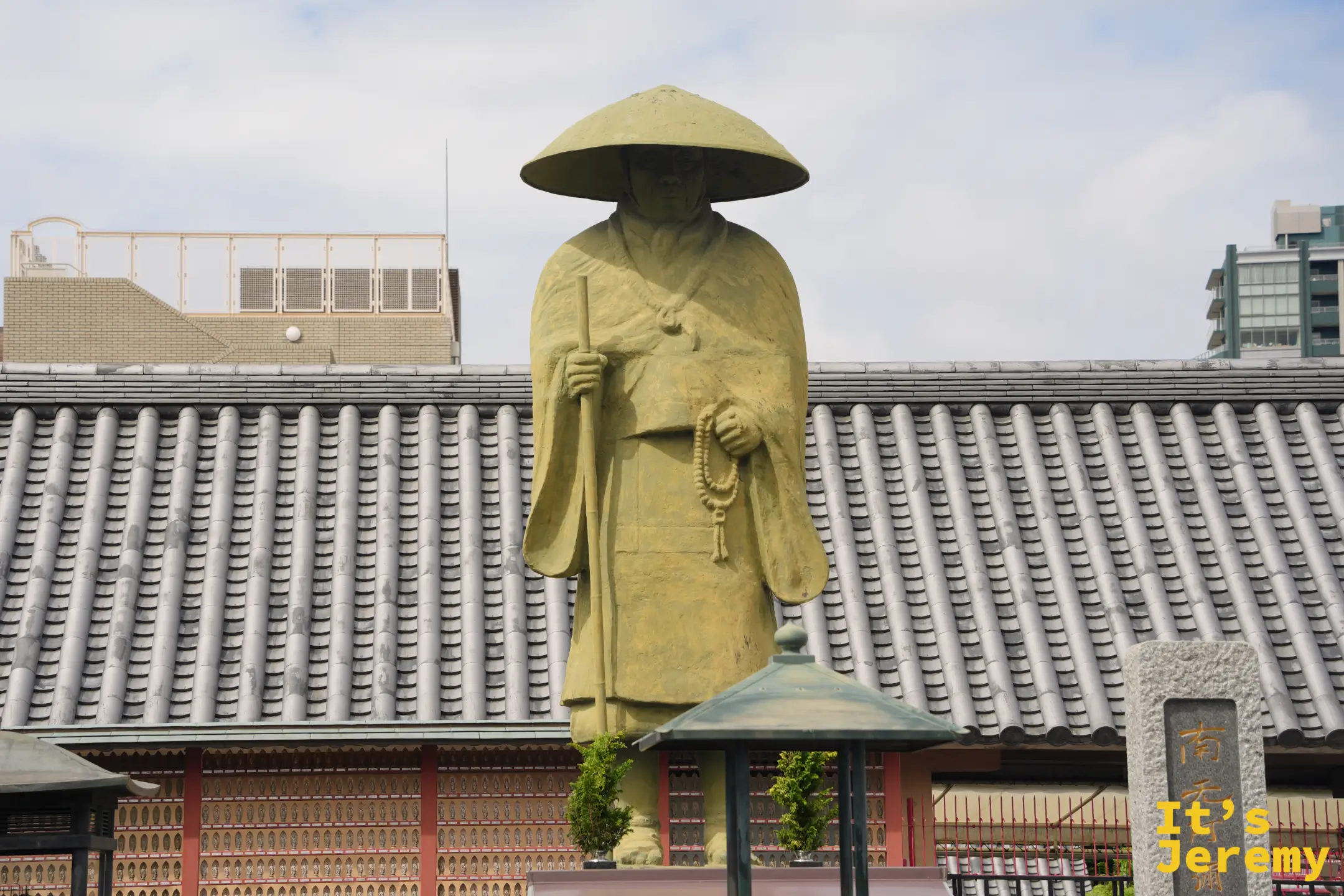 親鸞聖人像全身，站在瓦屋頂前方