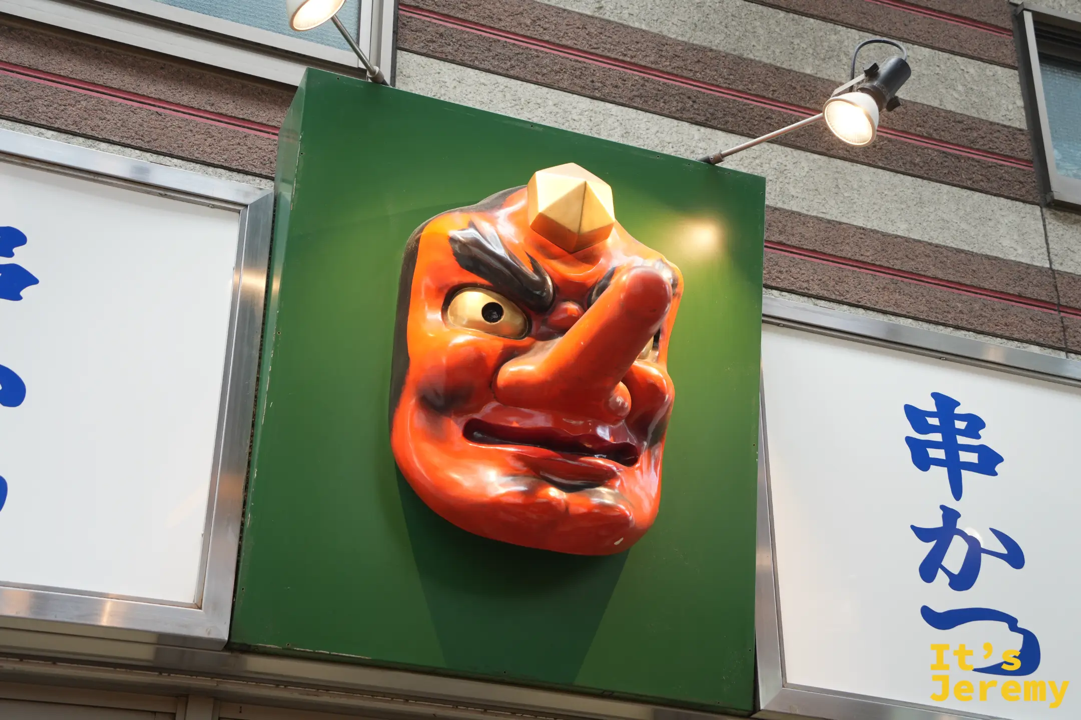 串炸店綠色招牌上的紅色天狗面具