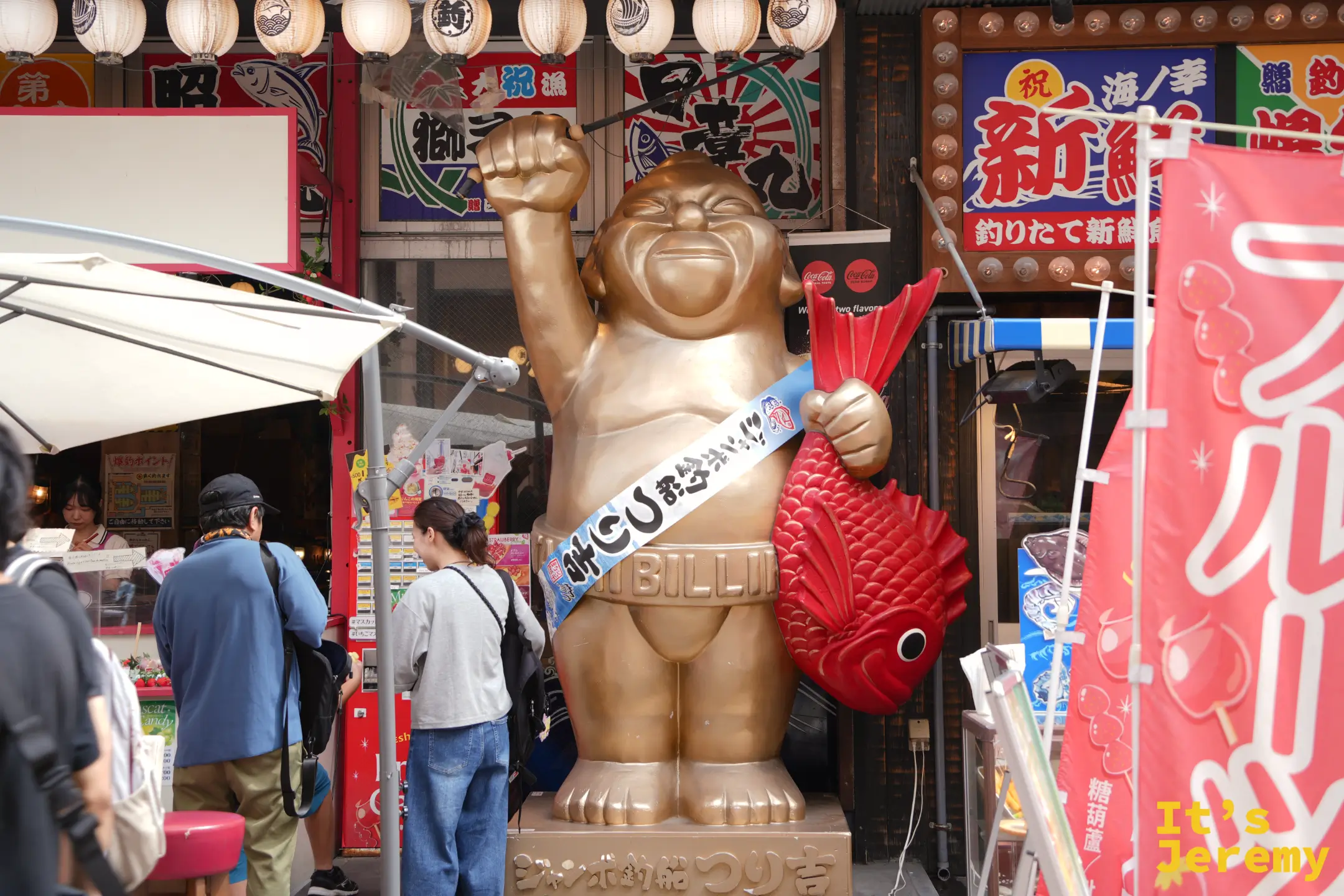 店門口舉著拳頭、抱著紅色鯛魚的金色比利肯